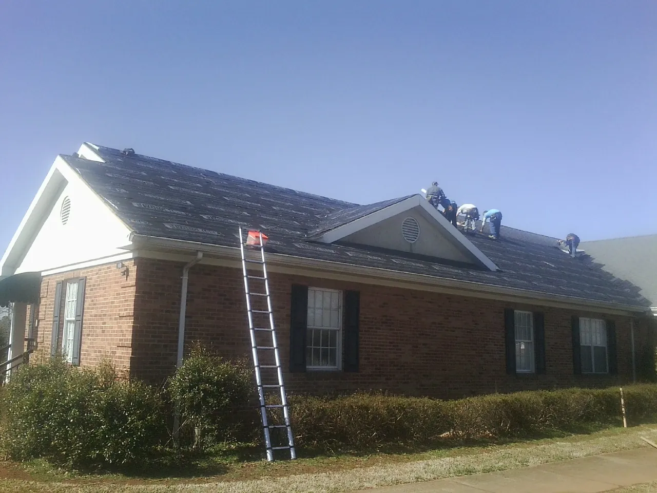 Crew tearing shingles off a brick ranch roof with a ladder set — Emergency Roof Repair work by our crew in Gurnee