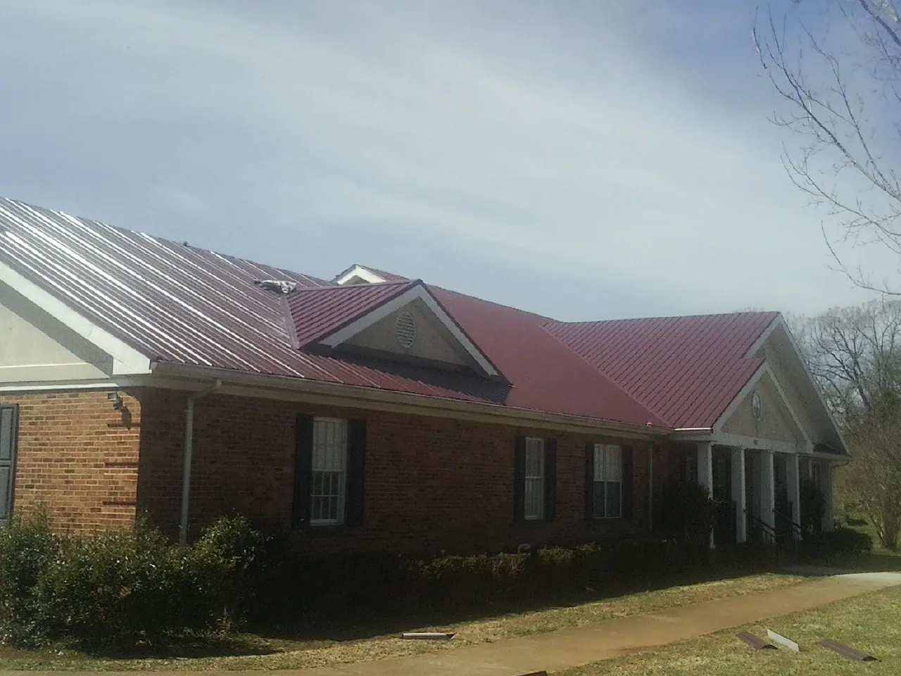 Red metal roof with gabled entries on a long brick building, from a Hail Damage Roof Repair job in Gurnee