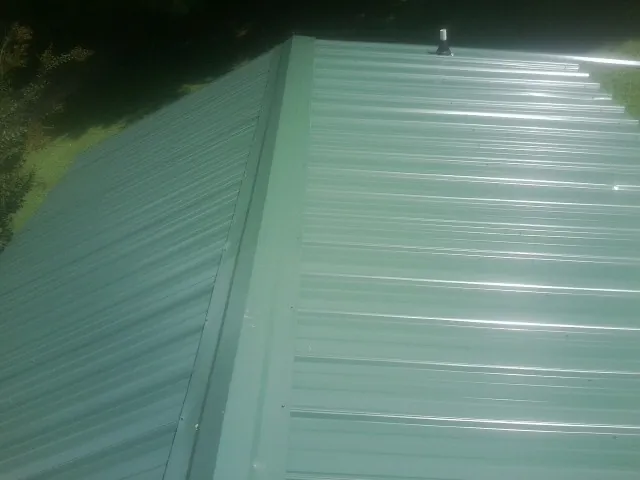 New green metal panels meeting at the ridge of a roof — Flat Roof Repair work by our crew in Gurnee