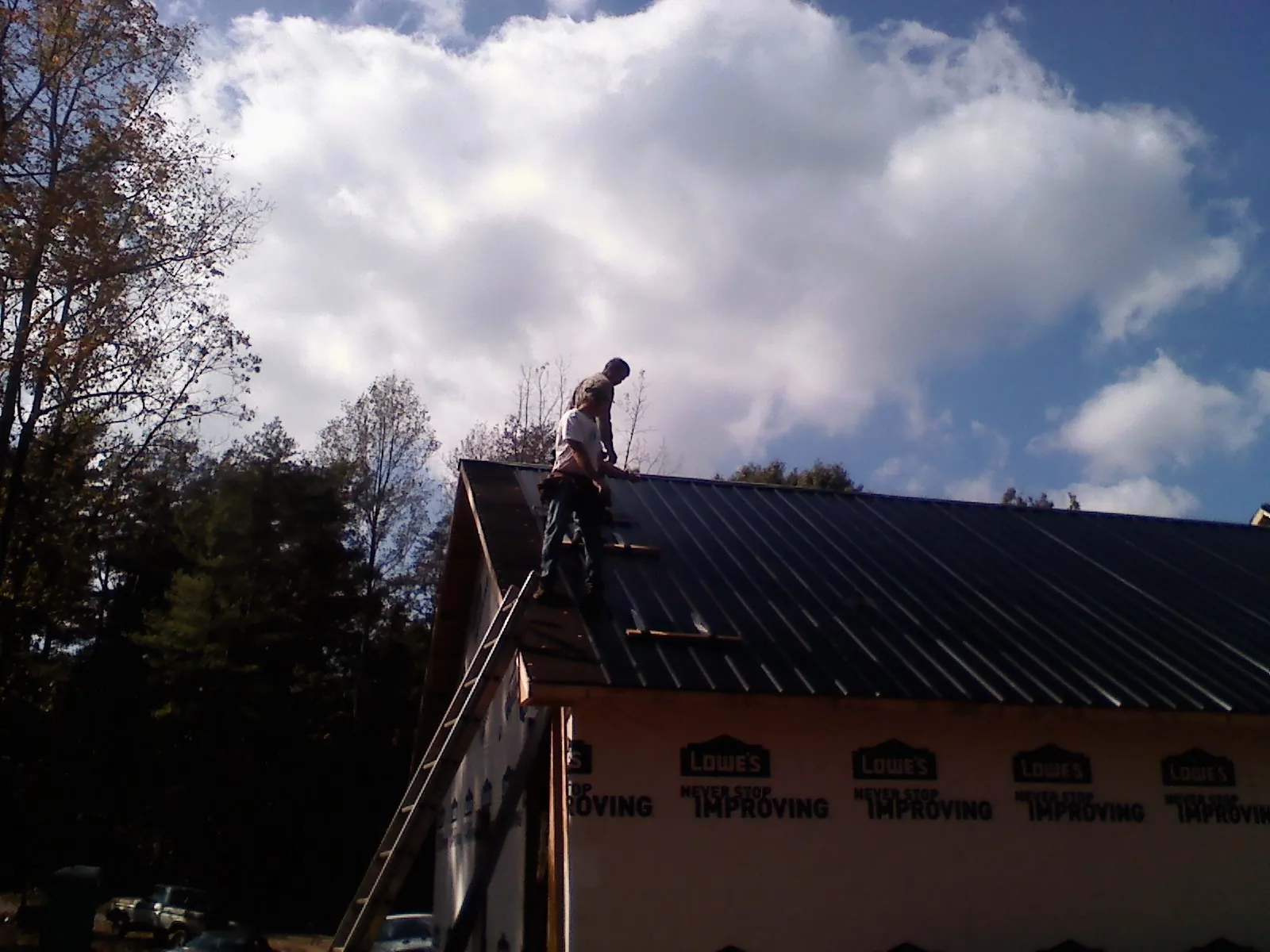 Roofer fastening dark metal panels high against a cloudy sky, from a Roof Inspection job in Gurnee