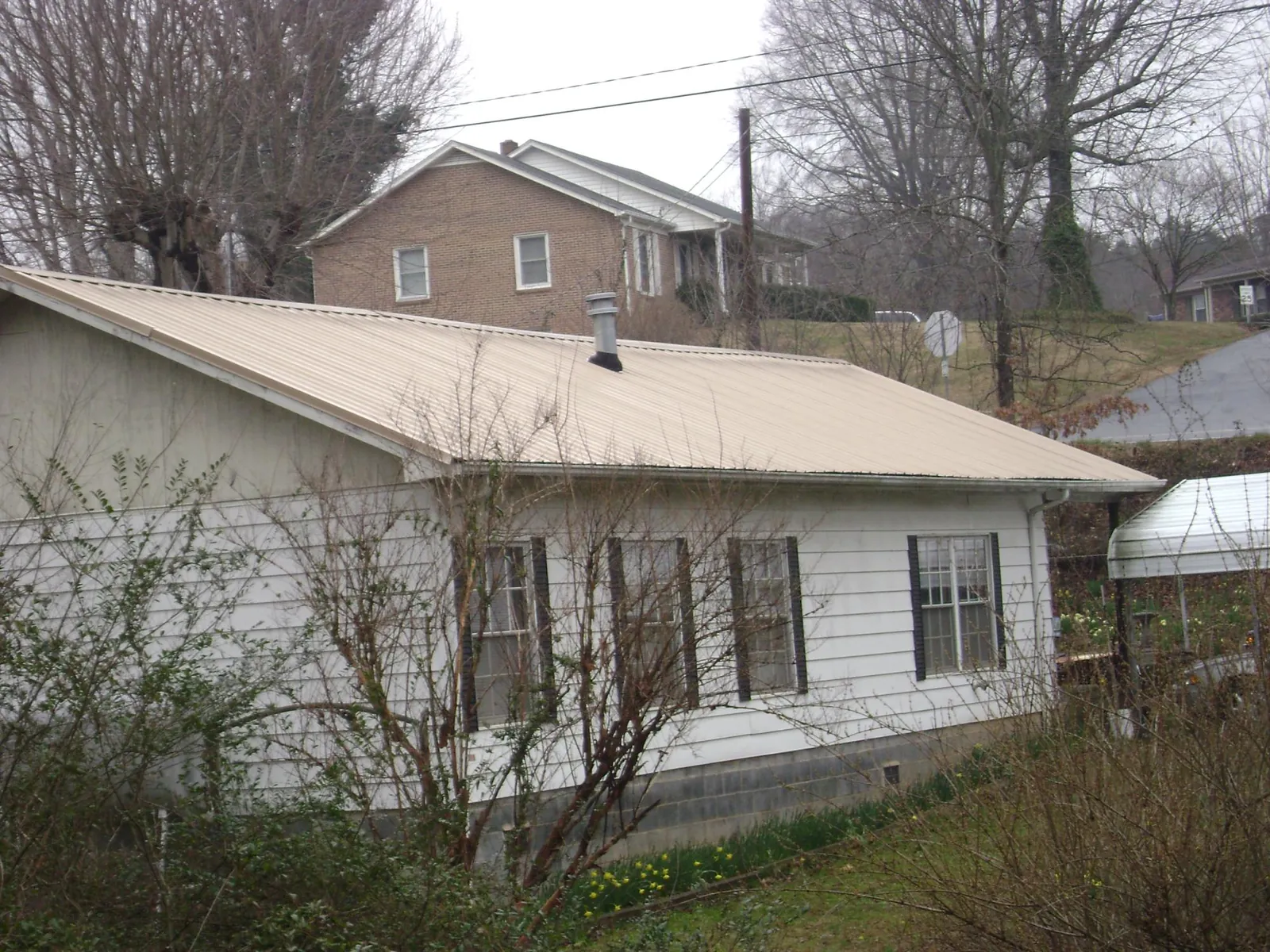 Tan metal roof on a white sided house set into a hillside — Commercial Roofing by Roofing Brothers in Gurnee